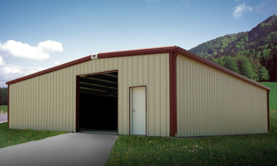 Ivory metal farm building with reddish-brown trim in a grassy meadow