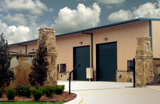 Attractive tan steel building with dark blue trim and native stone wainscot and entry gate