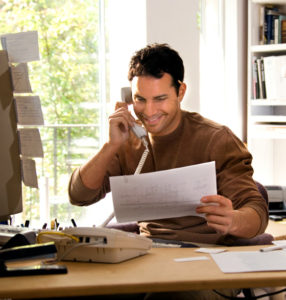 Photo of a man on the phone as he sits at a desk.