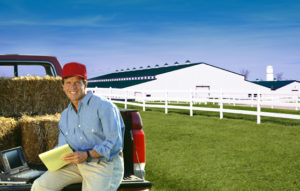 Happy young farmer sits on his truck before his beautiful steel barn building.