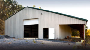 White steel barn with dark green trim and a shade shelter on the side.