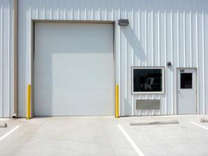 Photo of white metal building with an overhead door, entry door, and fixed glass window.